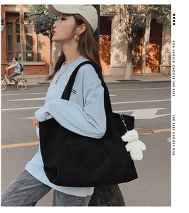 Detail view of a black corduroy tote bag with a cute white plush bear charm on a shoulder strap