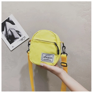 Close-up of a yellow canvas mini crossbody bag with black zipper and branded white label