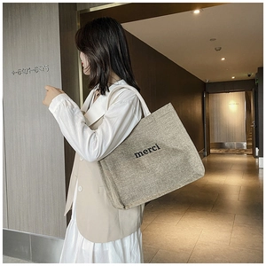 Detailed side view of large canvas tote bag with black merci print on linen material