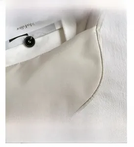 Macro shot of fine stitching and black button detail on a beige nylon crossbody bag