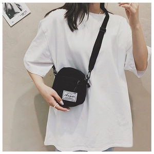 Close-up of a mini black canvas crossbody bag with adjustable strap and brand tag