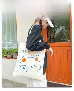 Detail shot of a white canvas tote bag with a minimalist blue cartoon bear and Hi text