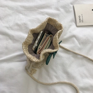 Handwoven straw bucket bag with green leaf appliques and white rope shoulder strap