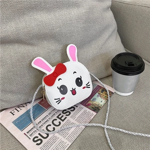 Detail shot of a white rabbit-shaped crossbody bag with pink ears and a red bow tie