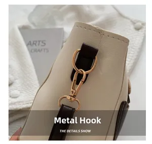 Detail of golden metal hook on beige leather bag with dark brown leather accents