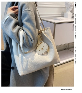 Detail view of white tote bag featuring embossed cartoon patterns and 3D bear pendant