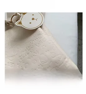 Detail of cream white tote bag with embossed cartoon bear patterns and leather charm
