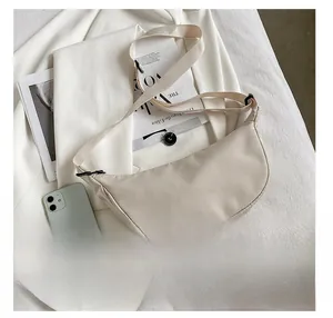 Top view of cream crescent crossbody bag with adjustable strap next to a mobile phone