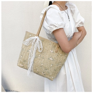 Detailed straw tote bag showing floral embroidery, lace bow, and leather handle strap