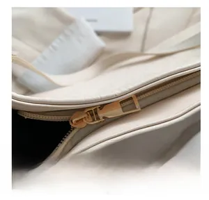 Detailed close-up of smooth gold zipper and embossed leather texture on cream tote bag