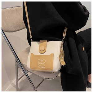 Detail of crossbody bucket bag with cartoon bear print and color-block styling on model