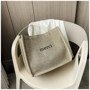 Detailed texture of burlap tote bag with black merci print on a modern chair