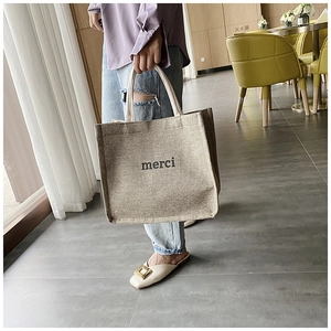 Close-up of beige linen tote bag featuring black merci text and woven texture
