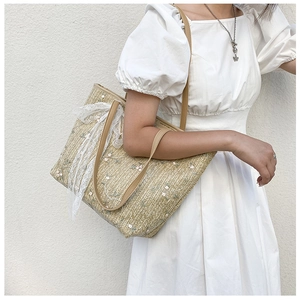 Detail of woven straw tote bag with floral embroidery and white lace ribbon bow