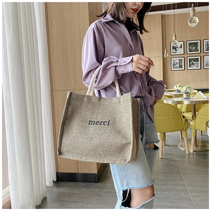 Detail view of khaki linen tote bag with merci print in a cozy cafe setting