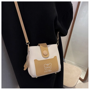 Detail of cream crossbody bucket bag with brown flap, wood button, and cartoon bear design