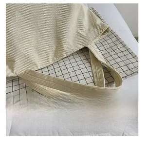 Close-up of reinforced shoulder straps on a beige corduroy tote bag with dual stitching