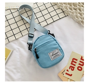 Detail of light blue canvas crossbody bag with adjustable strap and brand woven label