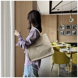 Detail of linen tote bag with merci print and white webbing straps in a cafe setting