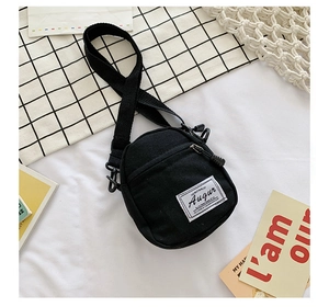 Detail of mini black canvas crossbody bag featuring adjustable strap and front logo patch