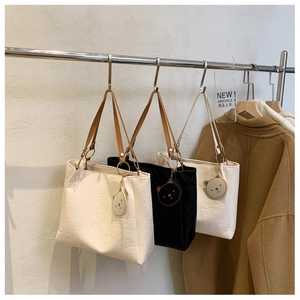 Detail of embossed tote bags in beige, black and white with cute bear head pendants