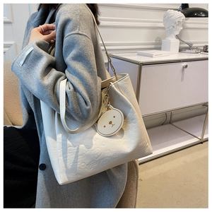 Close-up of white embossed tote bag with teddy bear patterns and matching bear charm