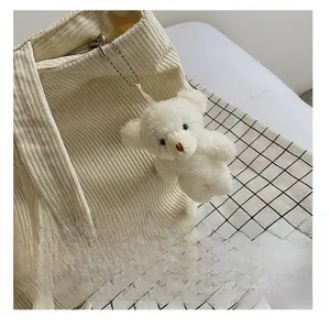 Detail of white plush bear charm hanging on beige corduroy tote bag with bead chain