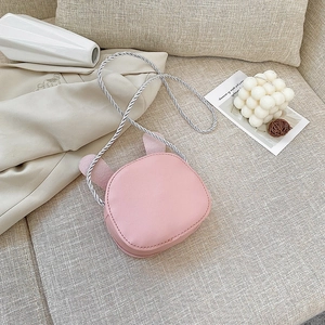 Cute pink crossbody child bag with rabbit ears and woven rope strap on beige sofa