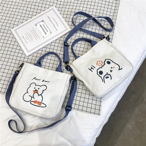 Detail of white canvas bags with cute bear prints, navy handles and adjustable straps