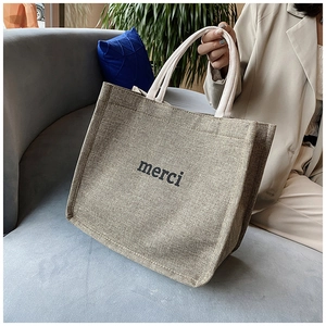 Detail of jute tote bag featuring merci print and cream woven handles in a lifestyle setting