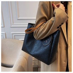 Close-up of black tote bag with embossed cartoon patterns and camel handles