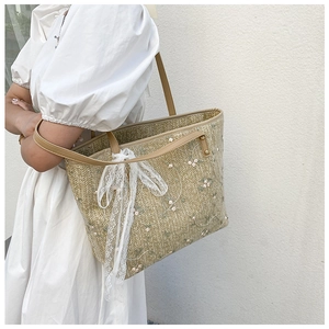 Lace straw tote bag with floral embroidery and brown leather handles on white background