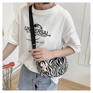 Detail of zebra pattern crossbody bag with cow charm and wide nylon strap shown in use