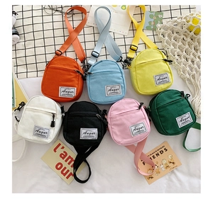 Flat lay of mini canvas crossbody bags in seven colors with adjustable straps and tags
