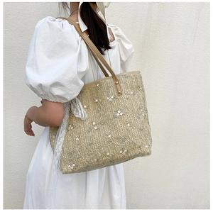Close-up of straw tote bag featuring floral embroidery and white lace ribbon detail