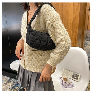 Detailed view of black quilted shoulder bag worn by model in a stylish interior setting