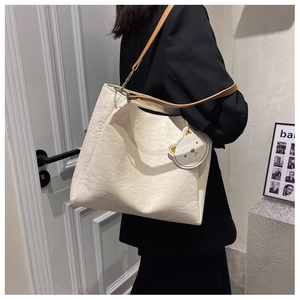Detail of off-white embossed tote bag featuring cartoon patterns and a cute bear charm