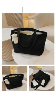 Detail of black corduroy tote bag with plush bear charm on white marble table