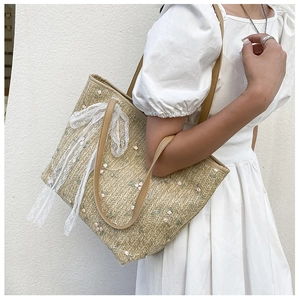 Detailed close-up of straw tote bag featuring floral embroidery and large lace bow