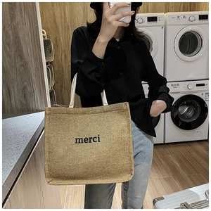 Close-up of a brown canvas tote bag featuring black 'merci' text and cotton handles