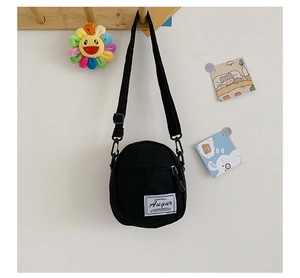 Detailed view of mini black canvas crossbody bag hanging on a hook with shoulder strap