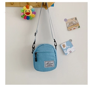 Detail of light blue mini canvas crossbody bag with adjustable strap and brand woven label