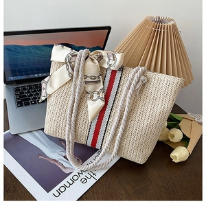 Detail of beige woven straw tote bag with cotton rope handles and decorative silk scarf