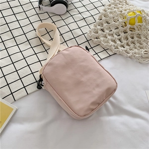 Top view of a small pink canvas crossbody bag with white adjustable straps on a bed