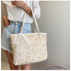 Detail of summer straw tote bag featuring floral embroidery and lace ribbon charm