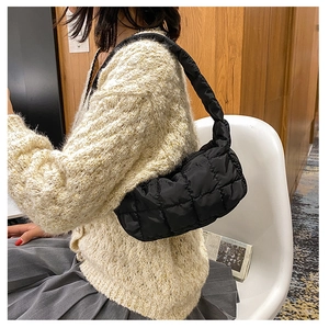Detailed side view of black quilted shoulder bag styled with beige knit cardigan