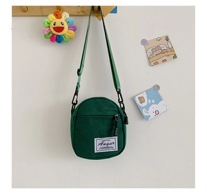 Close-up of dark green canvas crossbody bag featuring a front zipper pocket and strap
