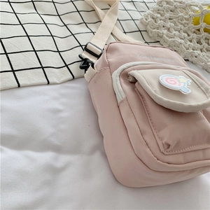 Close-up of pink crossbody bag with colorful lollipop badge and white woven strap