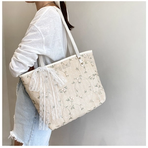Detail of floral embroidery on beige straw tote bag with white lace bow decoration
