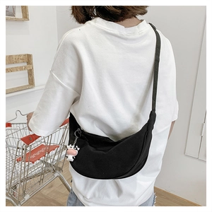 Detail of black canvas crescent bag with cow plush keychain and wide strap on a model